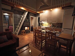 A cozy kitchen with a stone fireplace, wooden staircase, and a dining area with chairs and a table. - Tunturikoivu b1 by Interhome (Inari)
