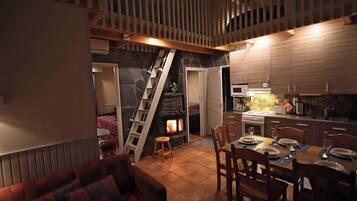 A cozy living room with a fireplace, a dining area with a table set for two, and a kitchen with modern appliances.
