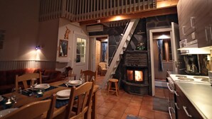Un interior acogedor con comedor, una escalera que sube a un altillo, chimenea y cocina.
