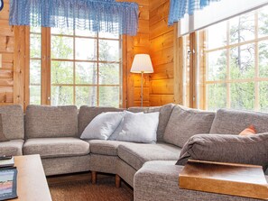 A wooden interior with a sectional sofa, a lamp, and large windows.