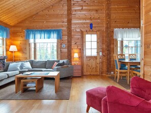 En hyggelig hytteinteriør med sofa, rød lænestol, spisebord og lampe.