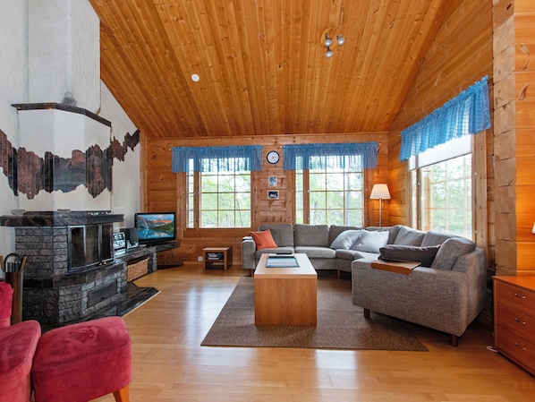 A cozy cabin interior with a fireplace, wooden walls, a sofa, and a television.