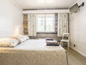 A room with a bed, a chair, a window with curtains, and a television on the wall. - Kiilopään maja by Interhome (Inari)