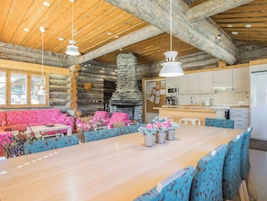 A spacious dining area with a long wooden table, blue upholstered chairs, and a stone fireplace.