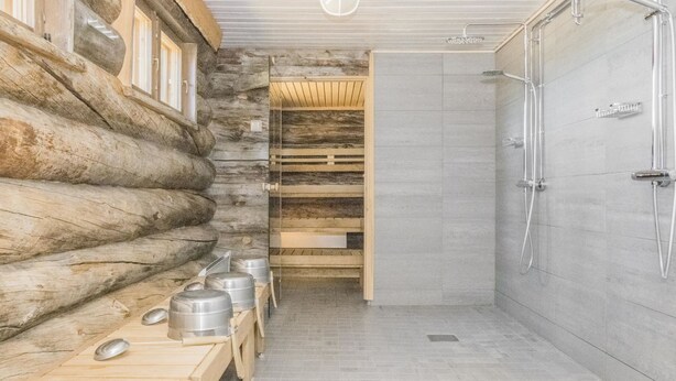 Ein Badezimmer in einer Blockhütte mit Dusche, Holzbanken und Metallbehältern.