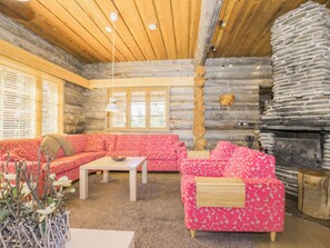 A log cabin interior with a sofa set, a fireplace, and a window with blinds.