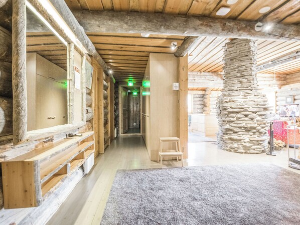 A corridor with wooden walls and a stone pillar, leading to a room with a stone fireplace.
