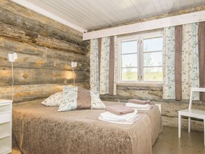 A log cabin bedroom with a bed, pillows, a chair, and a window with curtains.