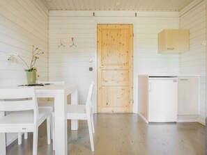 A room with a wooden door, white furniture, a small white refrigerator, and a green vase with flowers. - Kiilopään maja by Interhome (Inari)