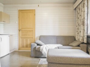 A room with a wooden door, a grey sofa, a white ottoman, and a patterned curtain. - Kiilopään maja by Interhome (Inari)