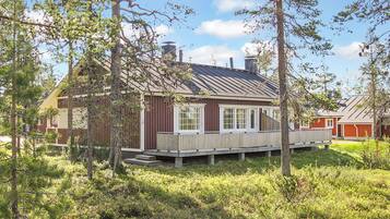 A wooden cabin with a deck, surrounded by trees and grass.
