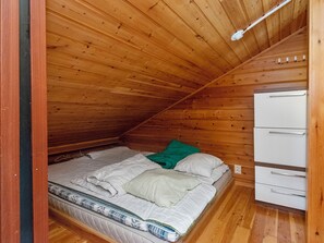 Une petite pièce aux murs lambrissés, avec un lit simple, une armoire blanche et un plafond en pente.