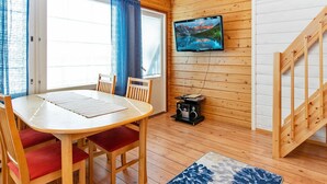 L’intérieur chaleureux d’un chalet, avec un revêtement mural en bois, une table à manger entourée de chaises, un téléviseur fixé au mur et un escalier.