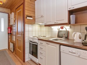 Cocina compacta con muebles blancos, estufa, horno, lavaplatos y fregadero.