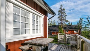 Une terrasse en bois avec une table de pique-nique et des bancs, un bâtiment rouge aux volets blancs et un ciel dégagé.