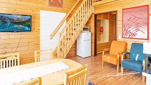 L’intérieur d’une cabane en bois comprend un coin repas, un escalier, un téléviseur et un réfrigérateur.
