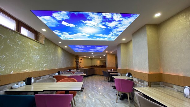 Un interno ristorante moderno con proiezione sul soffitto di cielo azzurro e nuvole, pavimento in marmo e sedie colorate.