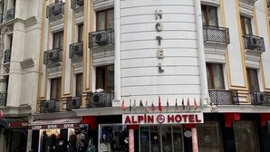 Un hotel con un cartello ben visibile che riporta la scritta "ALPIN HOTEL" e una facciata con balconi dotati di ringhiere elaborate.