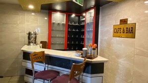 Zona caffè e bar con bancone in marmo, due sedie ed scaffali con bicchieri.