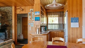 Un accogliente interno di una baita con un tavolo da pranzo in legno, sedie, angolo cottura e un camino in pietra.