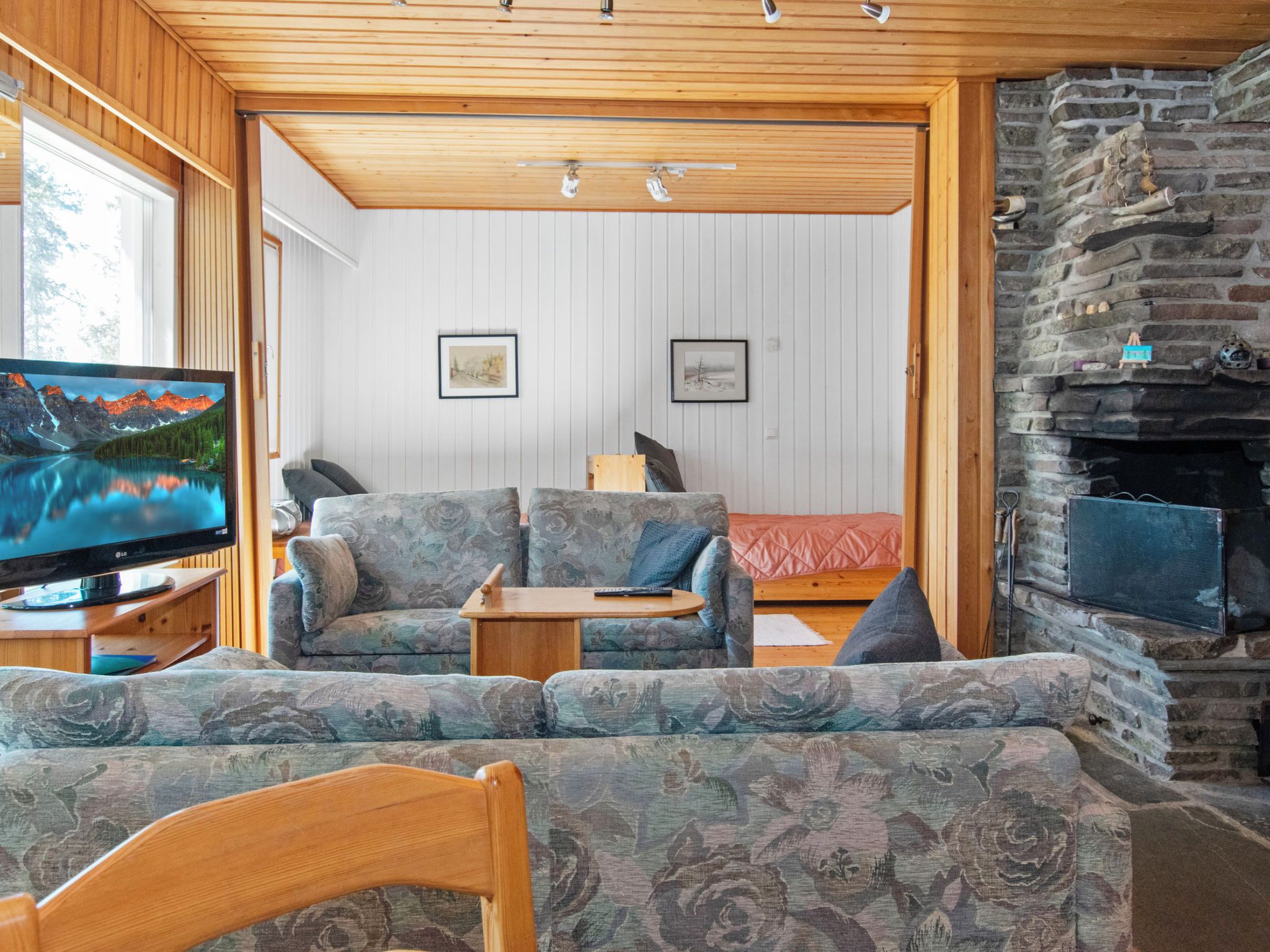 Una sala de estar acogedora con televisor, sofás estampados, una mesa de centro de madera y una chimenea de piedra.