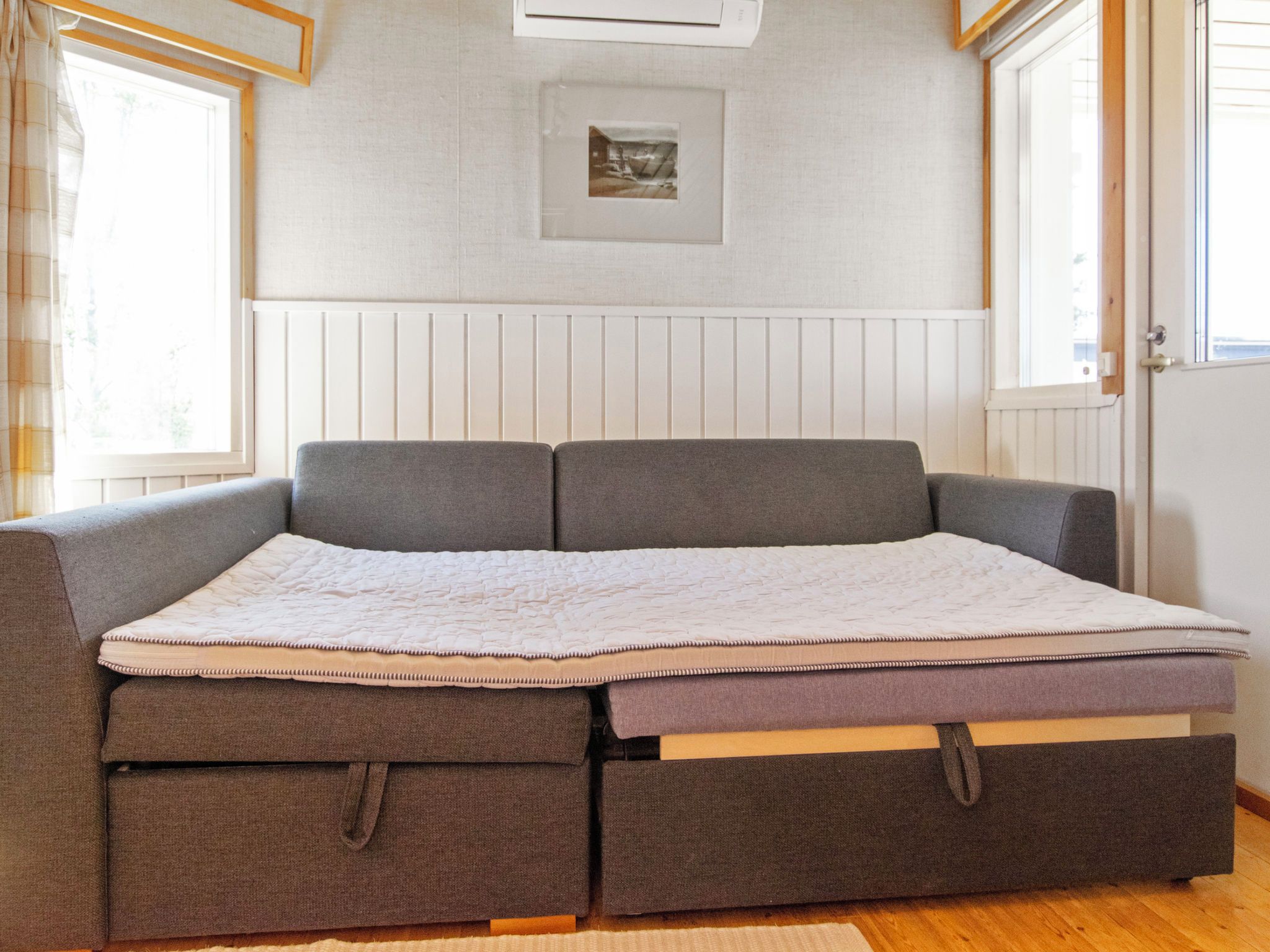 A sofa bed with storage drawers, a quilted mattress, and a framed picture on the wall.