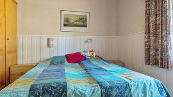 A bedroom with a bed, a pillow, a bedside lamp, a framed picture on the wall, and a window with curtains.