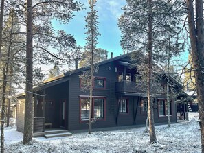 Une cabane moderne à l’extérieur sombre, dotée de grandes fenêtres et d’un balcon.