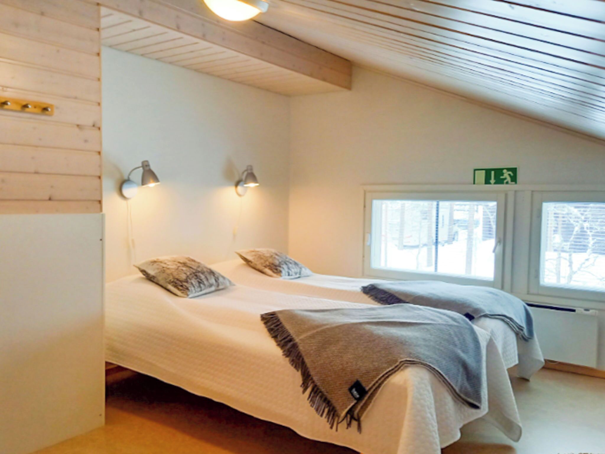 Une chambre avec deux lits, des poutres apparentes en bois au plafond, des appliques murales et une fenêtre offrant une vue.