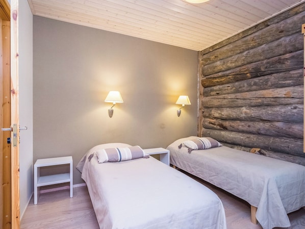 Una habitación con dos camas, una mesita de noche pequeña y una pared de troncos de madera.
