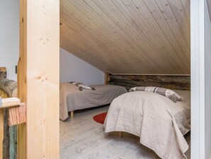 A small, cozy attic bedroom with two beds, wooden beams on the ceiling, and a red rug on the floor.