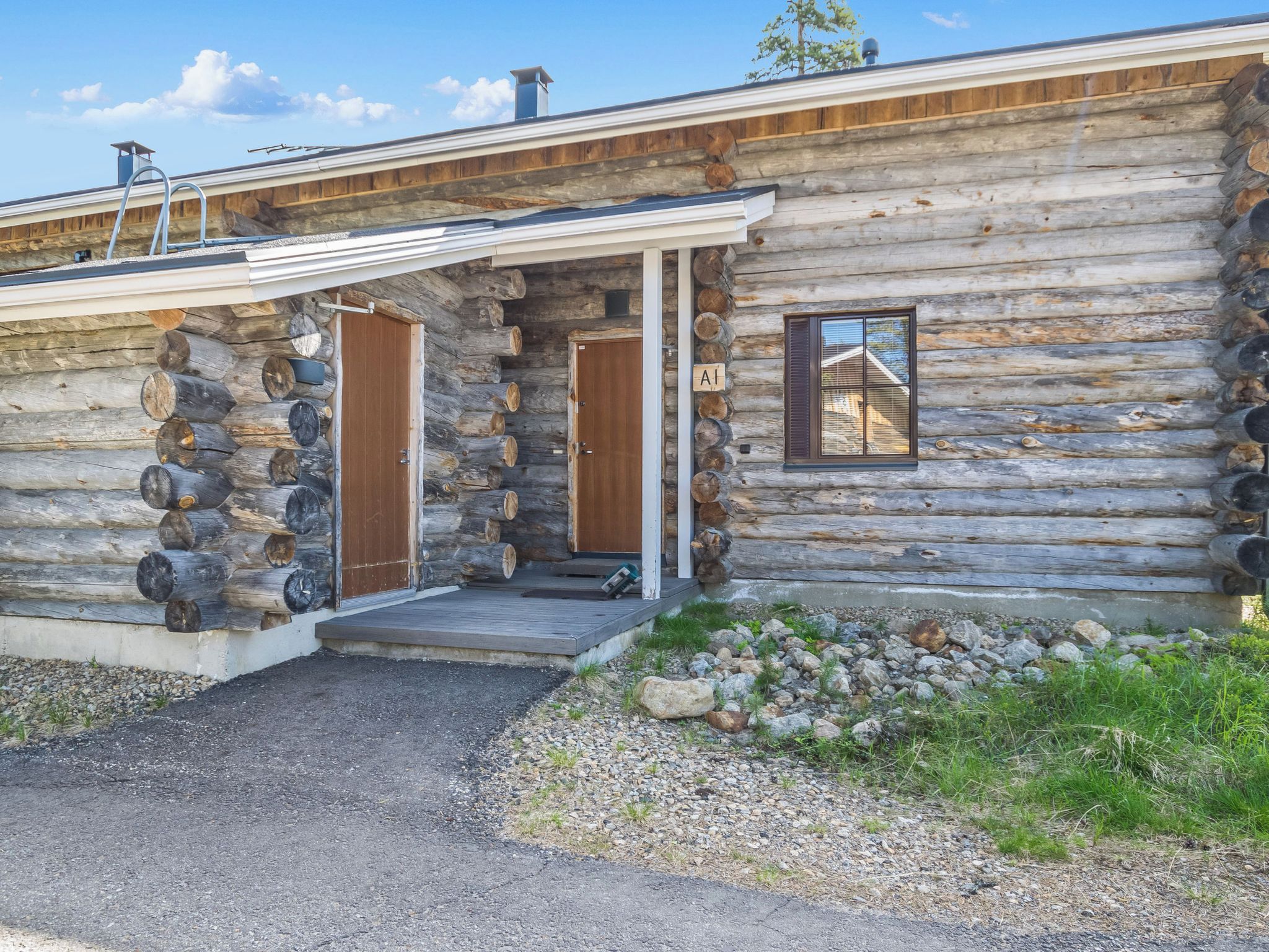 A log cabin with two wooden doors, a small window, and a porch with a metal railing.