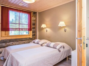 A bedroom with two beds, a window with red curtains, and two wall-mounted lamps.