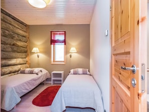 Una habitación con dos camas, una mesita y un ventanal con cortinas.
