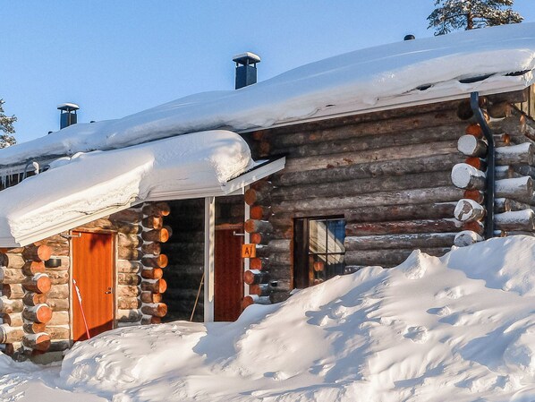 A log cabin with a snow-covered roof, wooden walls, and two visible doors.