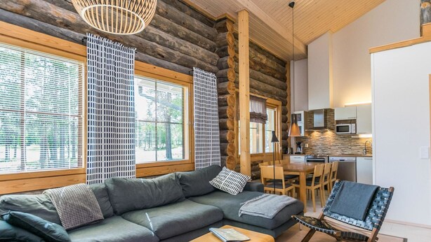Interior moderno de una cabaña de troncos con sofá gris, mesa de centro de madera y un comedor con una silla.