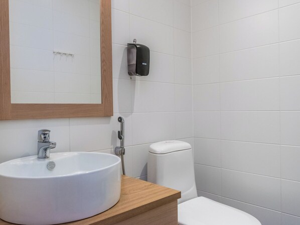 A bathroom with a white sink, a mirror, a toilet, and a soap dispenser.