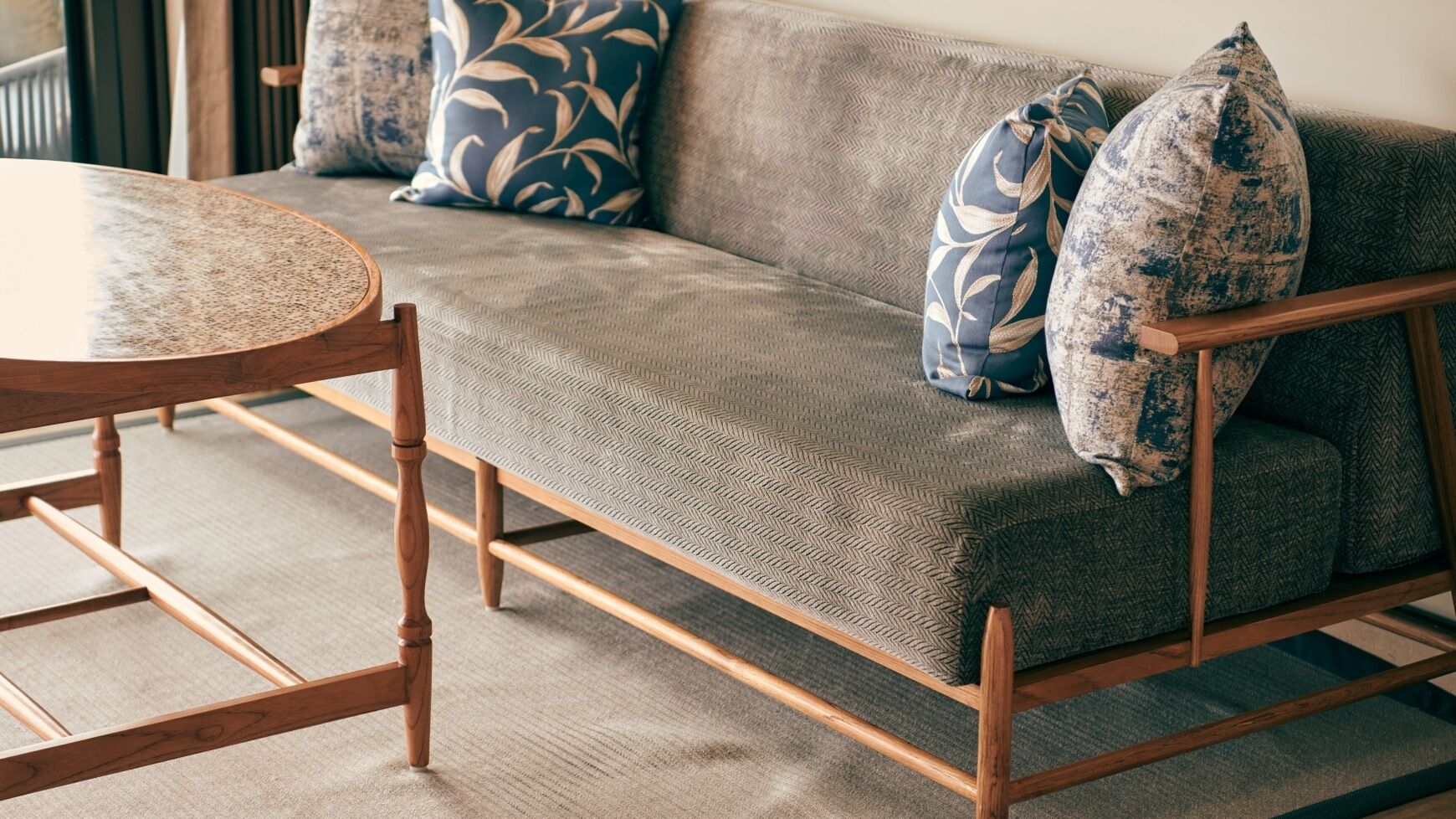 A sofa with a herringbone-patterned fabric, wooden legs, and decorative pillows with leaf designs.