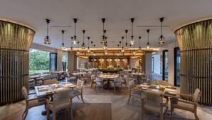 A spacious dining area with multiple tables and chairs, a central bar area, and large windows providing natural light. - AYANA Segara Bali (Jimbaran)