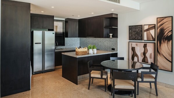 A modern kitchen with dark cabinetry, a stainless steel refrigerator, granite countertops, and a round dining table with chairs.