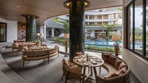 A spacious indoor area with wicker furniture, a pool, and a view of the pool and greenery. - AYANA Segara Bali (Jimbaran)