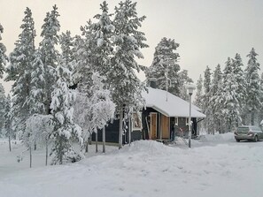 A snow-covered cabin with a wooden exterior, surrounded by snow-laden trees.