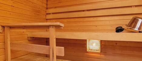 Una sauna con bancos de madera y un recipiente metálico en la pared.