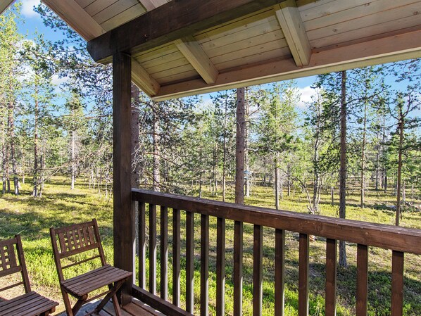 A wooden deck with a railing, two wooden chairs, and a view of a forested area.