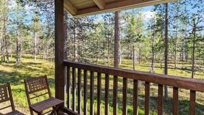 A wooden deck with a railing, two wooden chairs, and a view of a forested area. - Kuksatie 7 a by Interhome (Inari)