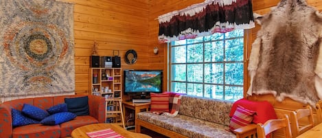 Interior acogedor de una cabaña con paredes de madera, televisor, sofá, mesa de centro y un ventanal grande.