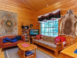 L’intérieur d’un chalet accueillant, avec un décor en bois, une télévision, un canapé, une table basse et une grande fenêtre.
