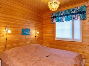 Une pièce de style cabane en bois, avec un lit, deux lampes fixées au mur, un tableau et une fenêtre avec un rideau.