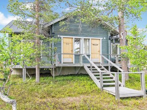 A wooden cabin with two doors, a wooden staircase, and a deck.