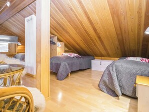 A cozy attic bedroom with two beds, a small table, and a chair.
